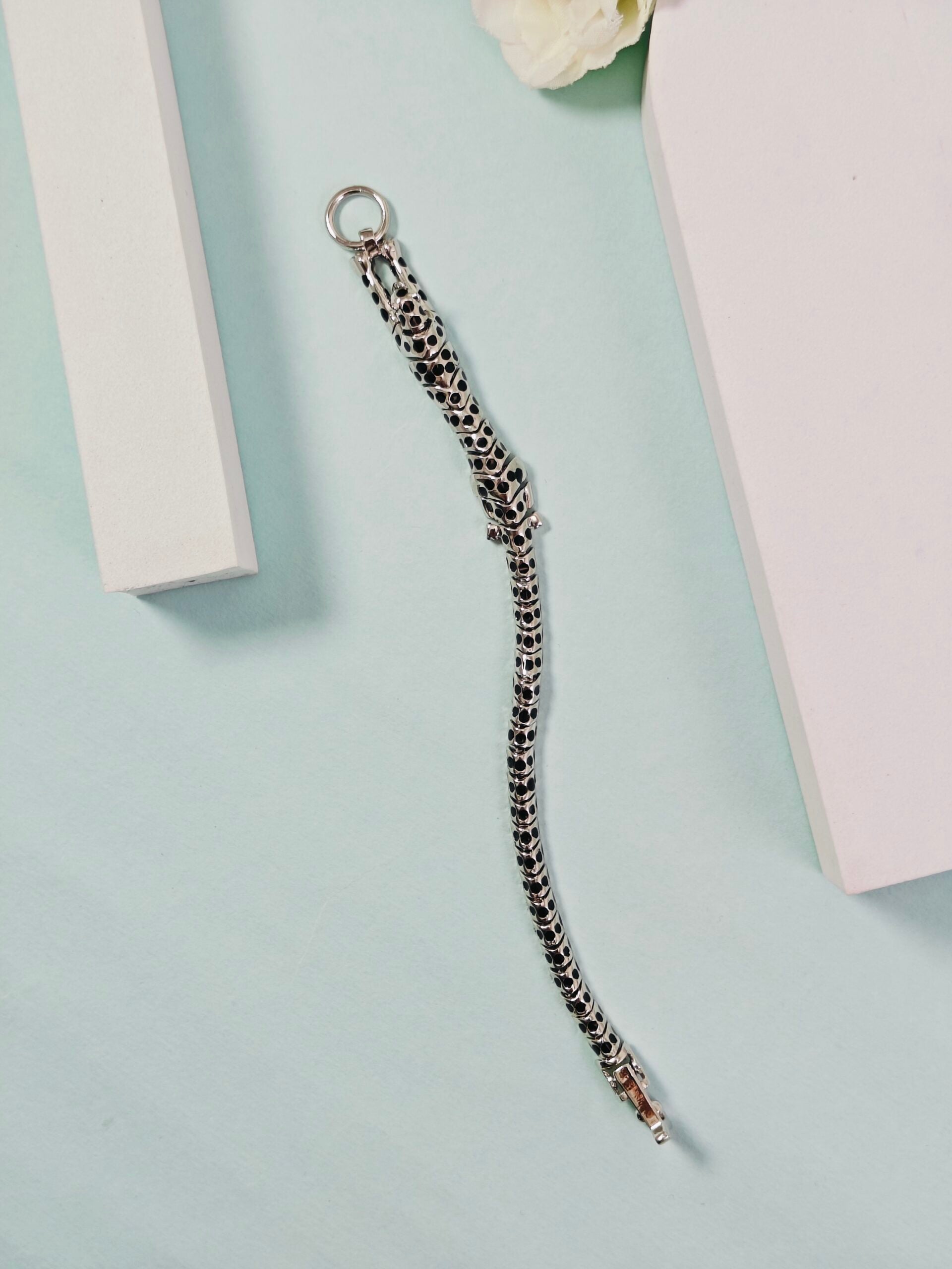 Silver chain bracelet on a light blue surface with a white flower and pink box in the background